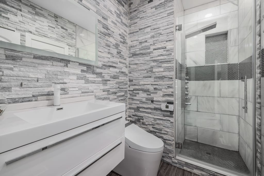 Modern bathroom with white vanity, glass walk-in shower and stone-clad wall
