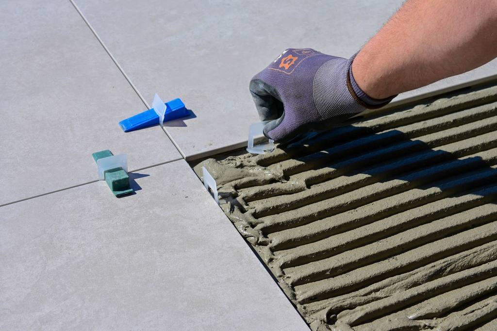 Tiler pressing levelling clips into a fresh adhesive bed between large porcelain floor tiles